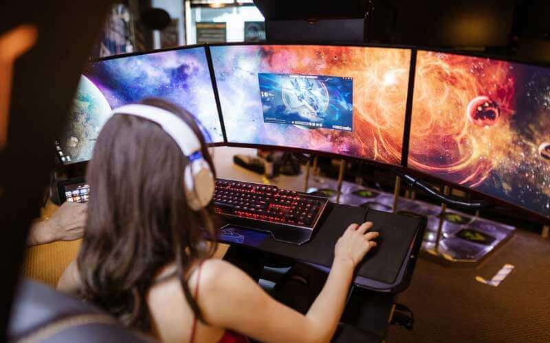 Chica jugando a un juego utilizando tres pantallas de un ordenador