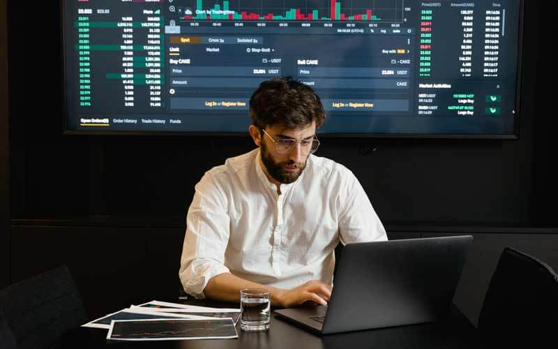 Hombre en una oficina trabajando con un ordenador y detrás gráficas proyectadas en una pantalla
