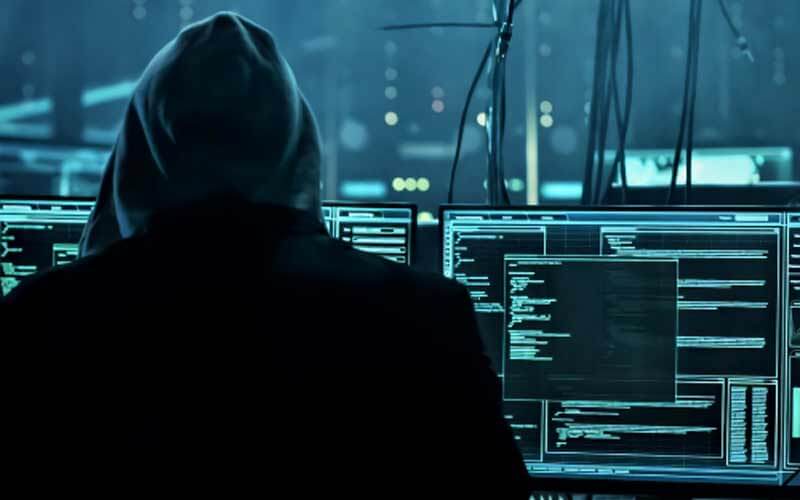 Hacker con varias pantallas de ordenador en una habitación oscura