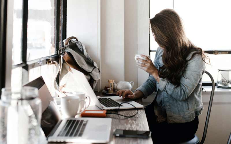 Chica con un café en una mesa larga con ordenadores